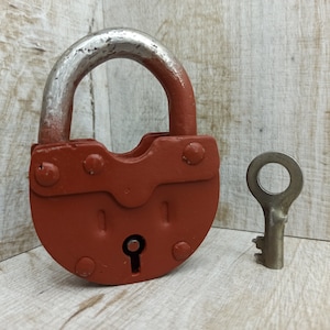 May include: A red padlock with a silver shackle and keyhole. The padlock has a silver key with a round bow.