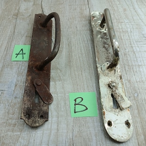 May include: Two antique door handles. Handle A is a rusty brown color, while handle B is painted white with a silver handle. Both have a long rectangular base with a curved handle and keyhole. The handles are displayed on a wooden surface.