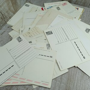 May include: A pile of vintage postcards, mostly cream-colored, with printed lines for writing. Some postcards have stamps and Cyrillic text. The postcards are arranged on a light-colored wooden surface, creating a nostalgic aesthetic.