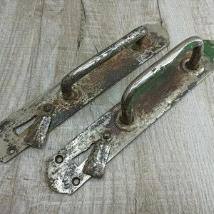 May include: Two antique door handles with a silver finish and a keyhole. The handles are made of metal and have a worn, aged look.