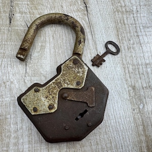 May include: An antique, open padlock with a matching key. The lock is a dark, rusty brown with a curved, arched shackle. The key is small and also shows signs of age. The lock has a decorative metal plate.