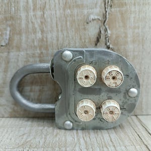 May include: A silver combination padlock with four dials, each with numbers from 0 to 9. The padlock has a U-shaped shackle and a metal body.