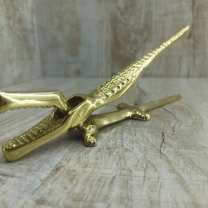 Può includere: Un schiaccianoci dorato a forma di alligatore con un design testurizzato dettagliato. Lo schiaccianoci è aperto, mostrando le mascelle pronte a rompere le noci.