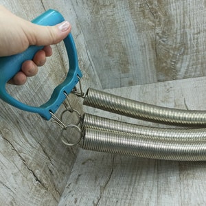 May include: A blue plastic handle with two silver spring coils attached. The coils are connected to the handle with metal rings.