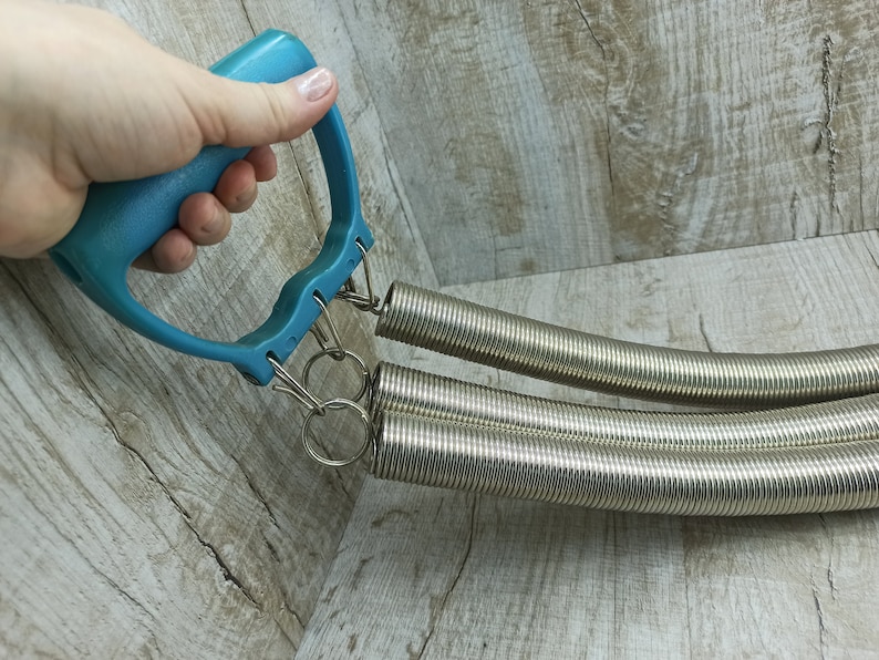 May include: A blue plastic handle with two silver spring coils attached. The coils are connected to the handle with metal rings.