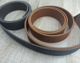 May include: Two leather straps, one black and one brown, are shown on a wooden surface. The straps are rolled up and are different widths.