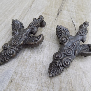 Puede incluir: Dos tiradores de cajón antiguos de color bronce con un diseño de pájaro ornamentado y estilizado. Cada tirador presenta una forma de pájaro con alas detalladas y patrones arremolinados, ideal para añadir un toque vintage a los muebles.