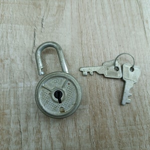 May include: A silver padlock with a round body and a keyhole. Two silver keys are attached to a ring.