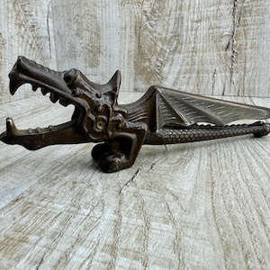 May include: A cast iron dragon nutcracker with wings outstretched and a detailed design. The nutcracker is painted in a dark brown color.
