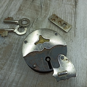 May include: A vintage padlock with two keys. The padlock is made of metal and has a round shape. The keys are silver and have a simple design.