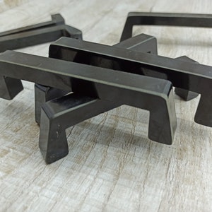 May include: A set of five black plastic drawer pulls. The pulls are all the same size and shape, and they have a simple, modern design.