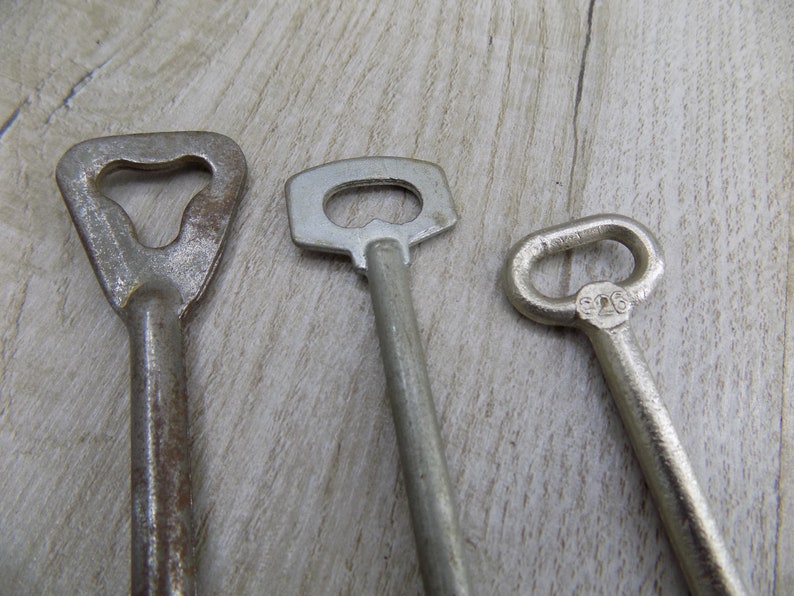 May include: Three vintage keys with different styles and finishes. The key on the left has a heart-shaped head and a rusty finish. The middle key has a simple, rectangular head and a silver finish. The key on the right has a round head and a silver finish with the number "316" engraved on it.