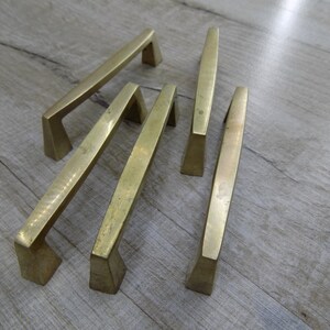 Op de afbeelding: Vier goudkleurige kastgrepen met een modern, geometrisch ontwerp. De grepen zijn gemaakt van metaal en hebben een geborstelde afwerking.