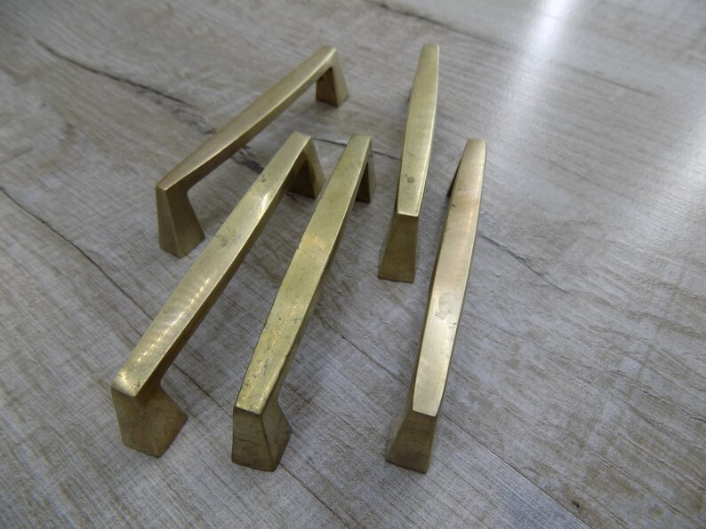 Op de afbeelding: Vier goudkleurige kastgrepen met een modern, geometrisch ontwerp. De grepen zijn gemaakt van metaal en hebben een geborstelde afwerking.