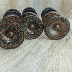 Peut inclure: Quatre boutons de porte ornés de style antique avec une finition cuivre et des motifs floraux complexes. Les boutons sont en métal et ont une base noire.