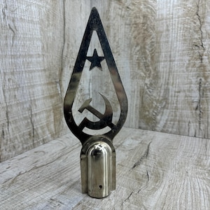 May include: A silver metal finial with a cutout design of a hammer and sickle and a star. The finial is attached to a round base.