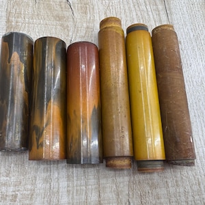 May include: Six different colored, round, wooden dowels. The dowels are all about the same length and have a smooth, polished finish. The colors are brown, black, orange, yellow, and gold.