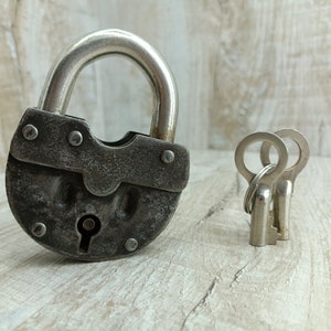 May include: A vintage padlock with a silver finish and two matching keys. The padlock has a worn, aged look and is made of metal.