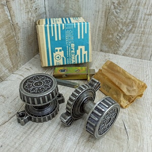 May include: Two antique silver door knobs with intricate floral designs. The knobs are on a wooden surface with a box labeled "ПЛАКА ВРЕЗНАЯ" in the background.