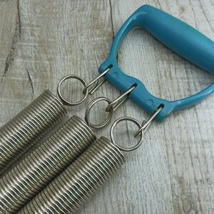 May include: A blue plastic handle with three silver spring coils attached. The coils are connected to the handle with silver rings.