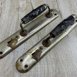 Puede incluir: Dos manijas de puerta antiguas con acabado plateado y empuñaduras facetadas negras. Las manijas tienen un ojo de cerradura y están montadas sobre una placa trasera rectangular. La ferretería muestra signos de desgaste.
