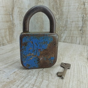 May include: A rusty blue padlock with a key. The padlock has the word "YUM" written on it.