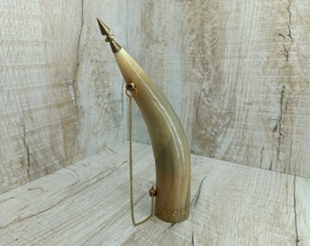May include: A decorative horn drinking vessel with a gold chain and a pointed top. The horn is made of natural material and has a brown and beige color.