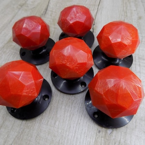 May include: Six red, faceted, plastic door knobs with black metal bases. The knobs have a textured, almost sparkly finish.