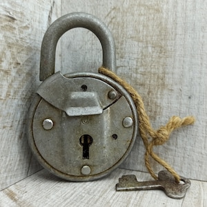 May include: A vintage silver padlock with a keyhole and a brown twine string attached to a key. The padlock has a round body with a circular keyhole and a small metal lever on the top.
