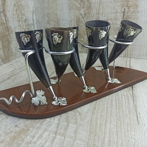 May include: Set of five black horn drinking cups with silver grapevine designs, displayed on a brown wooden stand with a silver scroll design.