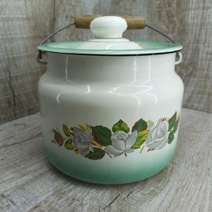 Könnte beinhalten: Weißer Emaille-Krug mit grünem Deckel und Blumendesign mit weißen Rosen und grünen Blättern. Der Krug hat einen Metallgriff mit einem Holzgriff.