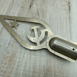 May include: A silver metal flag topper with a cut-out design of a star and hammer and sickle.