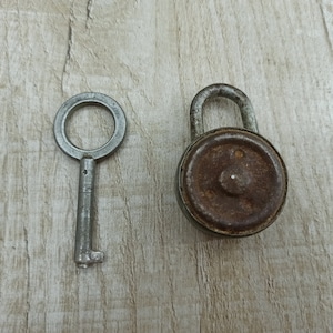 May include: A silver key and a rusty padlock with a round, metal body. The padlock is closed.