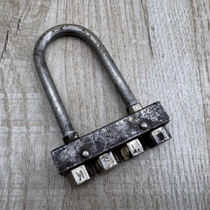 May include: A vintage combination padlock with a silver metal shackle and a black metal body. The padlock has a series of numbered dials that can be turned to open it.