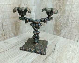 Puede incluir: Candelabro de bronce adornado con dos portavelas, que presenta un diseño floral detallado y una base cuadrada.