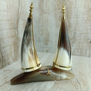 Pode incluir: Dois chifres decorativos com detalhes dourados e correntes, montados em uma base de madeira.