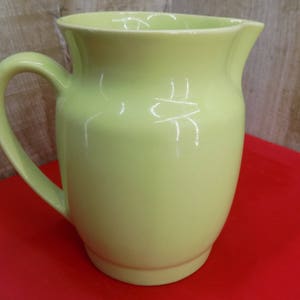 Może przedstawiać: Dzbanek ceramiczny w jasnożółtym kolorze z szerokim otworem i uchwytem. Dzbanek ma gładkie, błyszczące wykończenie.