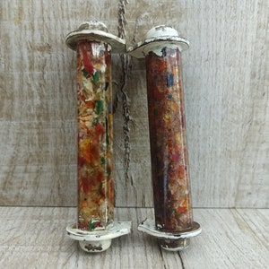 Könnte beinhalten: Zwei weiße, lackierte Holzspulen mit bunten Farbflecken auf der Oberfläche. Die Spulen haben an jedem Ende einen weißen Metallring.