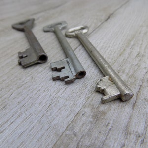 May include: Three antique keys with silver-toned metal finishes. The keys are arranged in a row on a light wood surface.