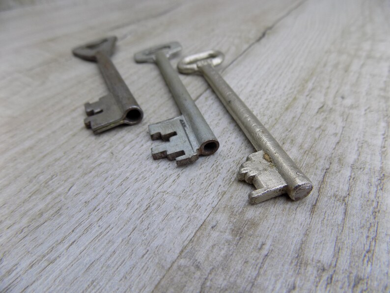 May include: Three antique keys with silver-toned metal finishes. The keys are arranged in a row on a light wood surface.