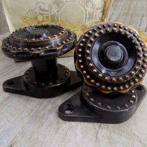 Könnte beinhalten: Zwei schwarze Türknauf mit kupferfarbenem Besatz und einem dekorativen Muster. Die Knäufe sind auf einer schwarzen Metallplatte montiert.