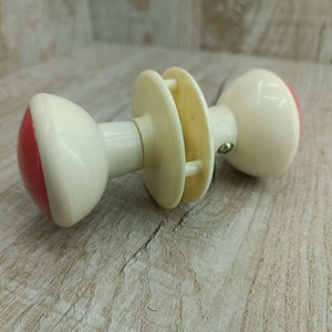 Può includere: Pomo per porta bianco con un accento rosso su un lato. Il pomo ha una forma rotonda e una vite in metallo.