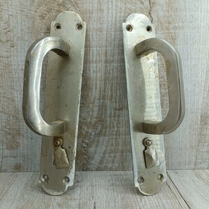 May include: Two silver door handles with a simple design. The handles are rectangular with a rounded top and bottom. The handles have a simple, curved design.