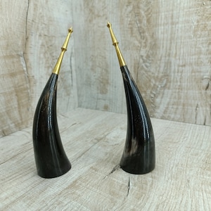 May include: Two black horn-shaped decorative objects with gold tops. The horns are polished and have a dark, rich color.