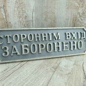 Può includere: Un cartello in metallo grigio con angoli arrotondati e lettere argentate che recita "СТОРОННИМ ВХОД ЗАПРЕЩЕН", che si traduce in "Ingresso vietato agli estranei".