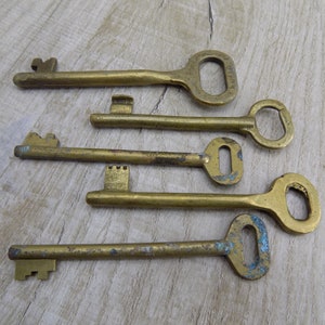 May include: Five antique brass keys with different shapes and sizes. The keys have a worn, aged look and are arranged on a light wood surface.