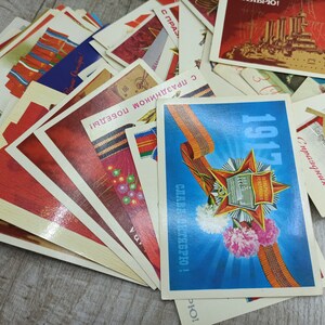 May include: A collection of vintage postcards with various designs and text. The cards feature red, blue, and white colors, with some showcasing military themes and historical imagery. The text includes dates and celebratory phrases.