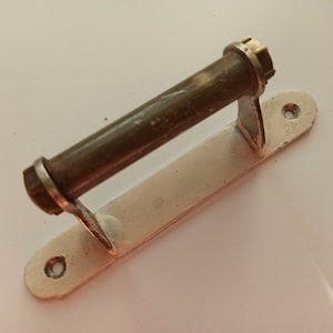 Pode incluir: Uma maçaneta de porta de metal branco com uma pega cilíndrica de latão. A maçaneta tem dois furos para montagem.