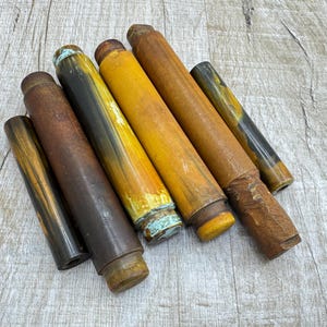 May include: Six cylindrical objects in shades of brown and yellow, with signs of wear. The objects have a weathered appearance, with some showing a mix of colours. They appear to be components of a larger item or decorative pieces.