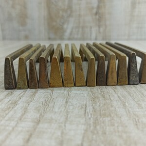 Op de afbeelding: Een set van 18 messing ladegrepen met een driehoekige vorm. De grepen zijn in een rij gerangschikt en hebben een licht verweerde afwerking.